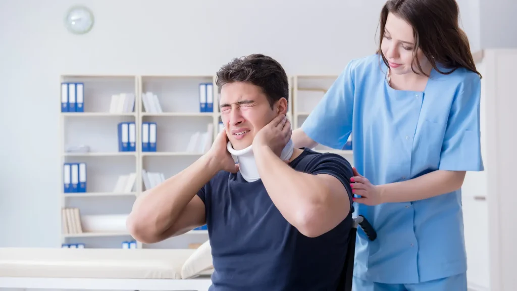 Man in neck brace holding his head in pain while being assisted by a healthcare worker.