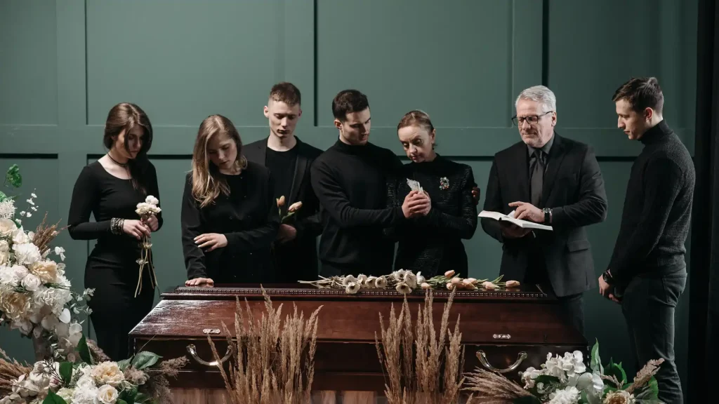 Group of people mourning beside a casket during a funeral service.