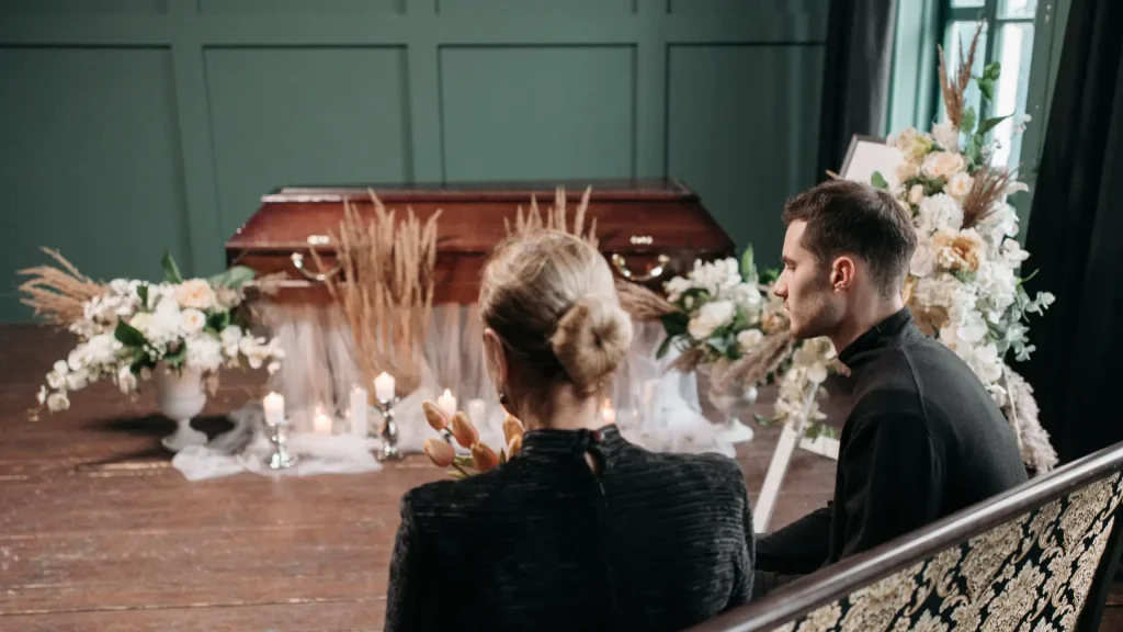 People sitting and facing a casket at a funeral service.