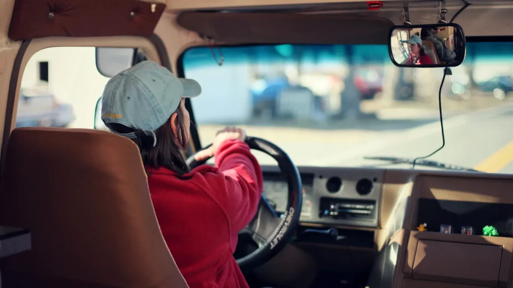 Person in a red shirt driving a vehicle, viewed from behind.