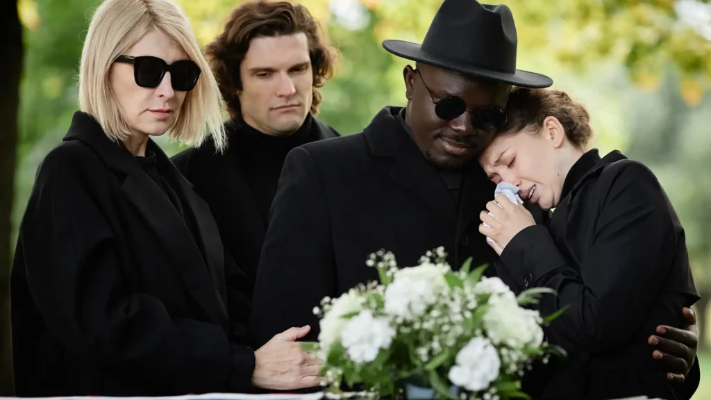 Mourners dressed in black grieving at funeral with flowers